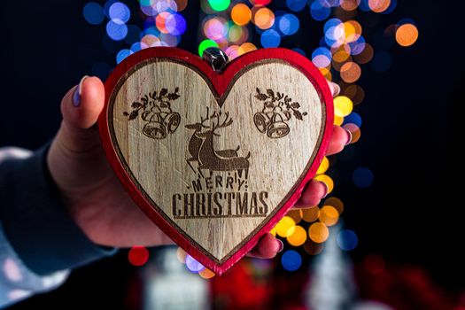 Holding Christmas heart shape decoration isolated on background with blurred lights. December season, Christmas composition.