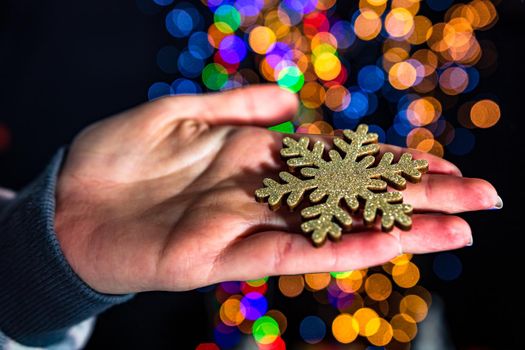 Holding Christmas snowflake decoration isolated on background with blurred lights. December season, Christmas composition.