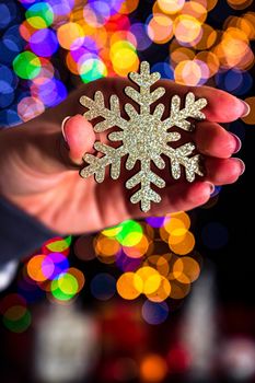 Holding Christmas snowflake decoration isolated on background with blurred lights. December season, Christmas composition.