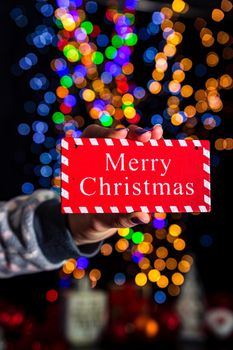 Holding Merry Christmas sign isolated on background with blurred lights. December season, Christmas composition.