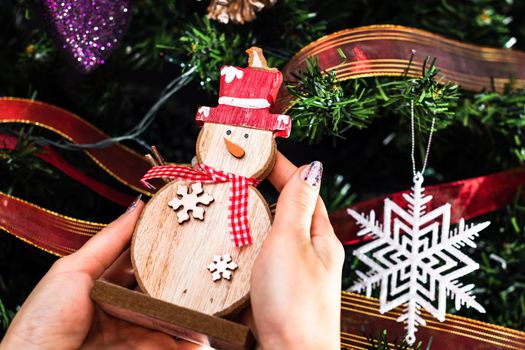 Hands holding Christmas snowman figurine in front of the Christmas tree. Decorating the fir tree isolated