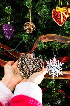 Hands holding Christmas ornament in front of Christmas tree. Decorating fir branches with Christmas decorations.