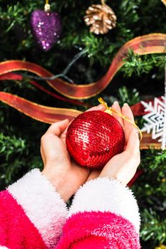 Hands holding Christmas ornament in front of Christmas tree. Decorating fir branches with Christmas decorations.