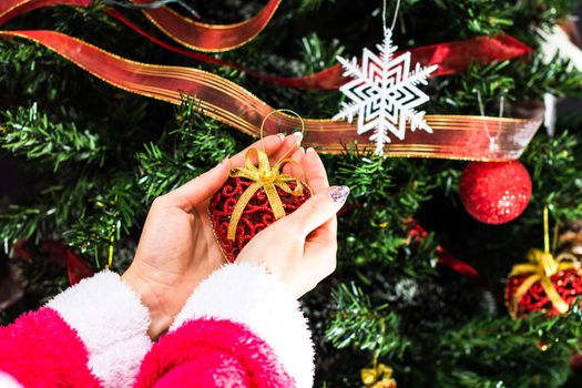 Hands holding Christmas ornament in front of Christmas tree. Decorating fir branches with Christmas decorations.