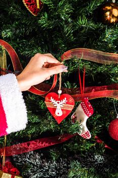 Decorating Christmas tree, hand putting Christmas decorations on fir branches. Christmas hanging decorations.