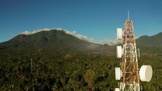 Telecommunication tower, communication antenna against mountains and rainforest, aerial view. Repeaters on a metal tower. Camiguin, Philippines