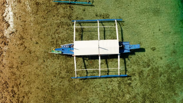 Traditional Philippine boat on the surface of the azure water in the lagoon. Top view of boat from drone.