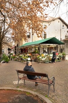 Udine, Italy. February 2 2021.  a man sitting on a bench in the winter season in a square in the historic center of Udine