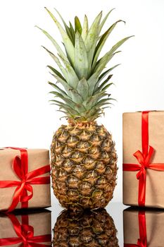 Fresh pineapple fruit and square gift boxes in craft paper on black glass table on white background