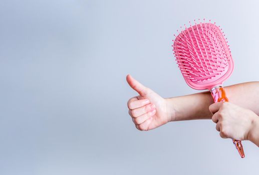 Beautiful pink comb brush in the hand of a girl with thumb up on white background. Women's Hair Care Accessories. Side view