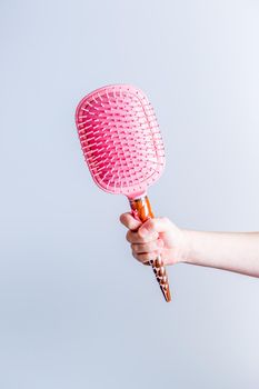Beautiful pink comb brush in the hand of a girl on a white background vertical. Women's Hair Care Accessories. Side view