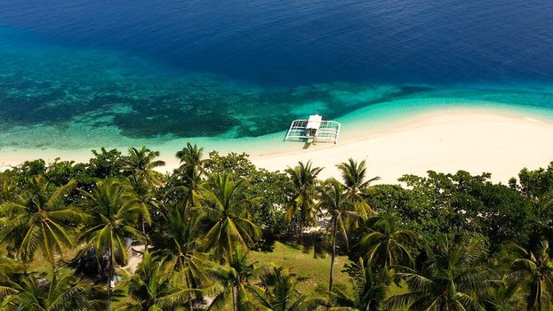 Tropical beach of white sand, top view. Tourist boat off the coast. Blue sea with turquoise lagoons. Summer and travel vacation concept. Tranquil beach scene.