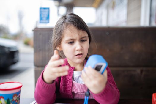 Cute and concerned-looking little girl in pink sweater holding small camera for kids. Adorable young child playing with toy camera with blurry background. Kids interacting with technology