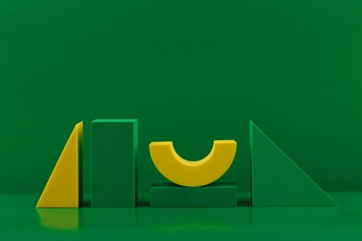 Abstract geometric composition with green and yellow figures on green glossy table with reflection against green background with copy space. 