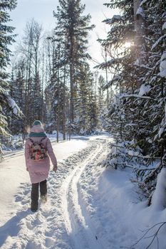 A girl in a red jacket walks through a snow-covered forest on a winter day. Rear view. A man on the background of a beautiful winter nature