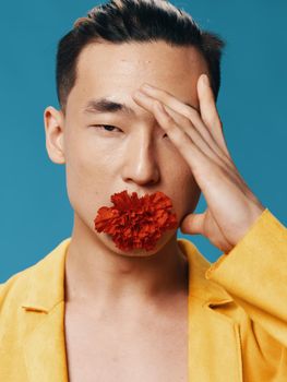 A man of Asian appearance touches his face with his hand and a red flower in his mouth. Close-up portrait. High quality photo