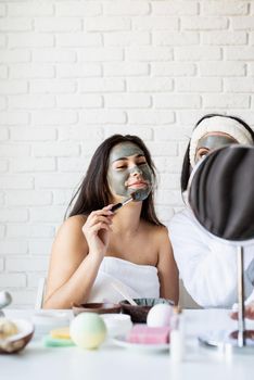 Spa and wellness concept. Self care. Portrait of a beautiful woman with long black hair applying facial mask doing spa procedures