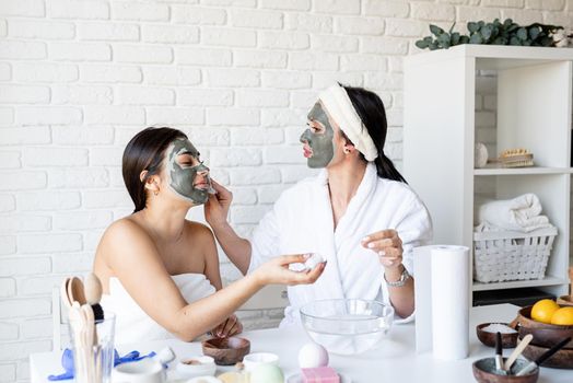 Spa and wellness concept. Self care. two beautiful women in bath robes applying facial mask having fun