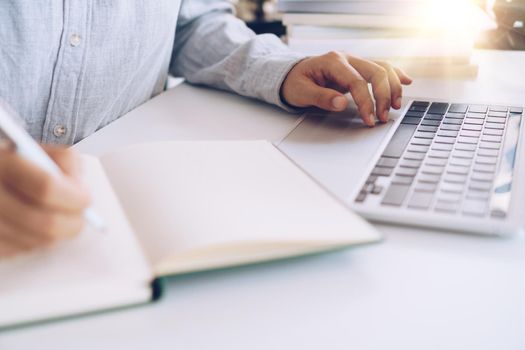 Woman is writing in planner notebook while using laptop to work or plan with workspace at home. Education business lifestyle concept.