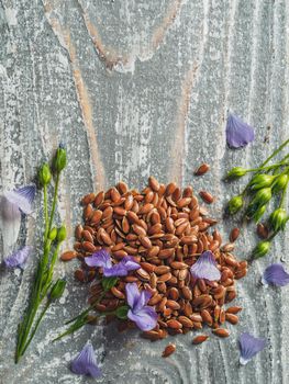 Flax seeds and flax oil. Brown linen seeds, flaxseed oil and blue flax flowers on old gray wooden background. Copy space. Vertical. Top view or flat lay.