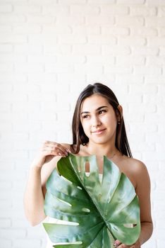 Spa Facial Mask. Spa and beauty. Happy beautiful brunette woman wearing bath towels holding a green monstera leaf in front of her face