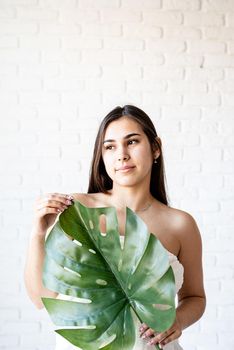 Spa Facial Mask. Spa and beauty. Happy beautiful brunette woman wearing bath towels holding a green monstera leaf in front of her face