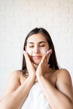 Spa and beauty. Happy beautiful caucasian woman wearing bath robes applying facial cream on her face