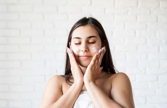 Spa and beauty. Happy beautiful caucasian woman wearing bath robes applying facial cream on her face