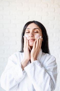 Spa and beauty. Happy beautiful middle eastern woman wearing bath towels applying facial cream on her face