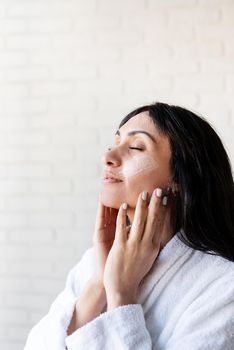 Spa and beauty. Happy beautiful middle eastern woman wearing bath towels applying facial cream on her face