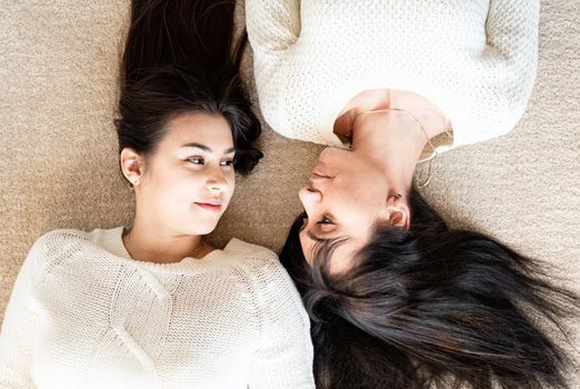 Two best friends laying on the rug at home talking, top view