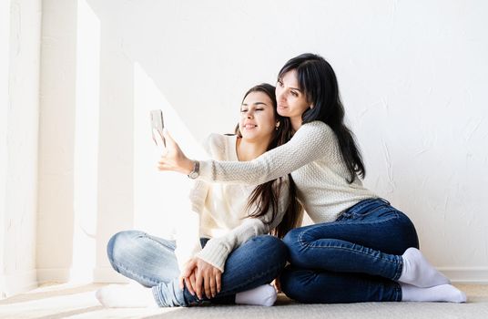 Two beautiful women friends taking selfie on mobile phone making funny faces
