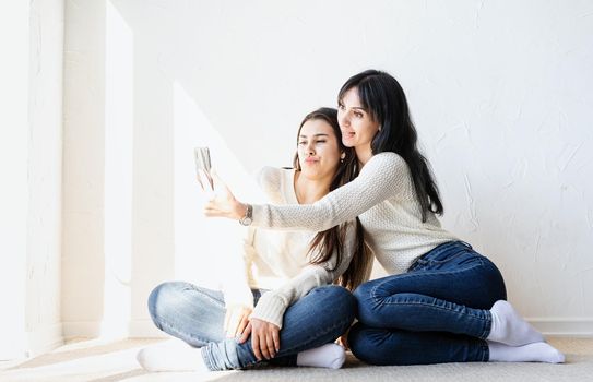 Two beautiful women friends taking selfie on mobile phone making funny faces