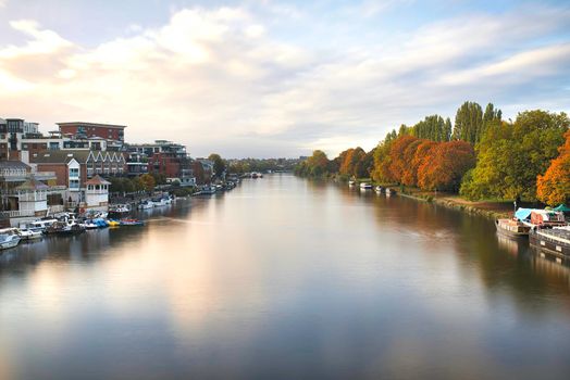 Aerial view of River Thames surrounded by buildings and autumn-colored trees and under beautiful sky. Majestic skyline above a forest and peaceful river. Tranquil autumn landscapes
