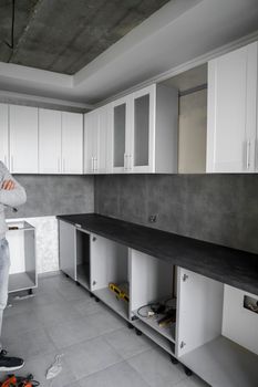 Custom kitchen cabinets installation with a white furniture facades mdf. Gray modular kitchen from chipboard material on a various stages of installation. A frame furniture fronts mdf profile