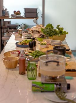 A kitchen with a cooking table in the middle of the room and the table is full of ingredients for cooking. The concept of a food healthy lifestyle. No focus, specifically.