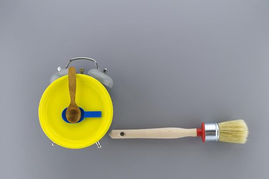 Creative DIY, decorating or renovations background with two clean bristle brushes and a colorful yellow alarm clock with tools for hands forming a border on grey with copy space