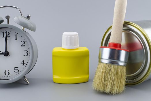 DIY, decorating or renovations concept with a still life of an alarm clock with assorted clean paint brushes and unlabeled tin of paint over a grey background