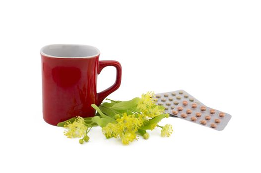 Red cup near freshly picked yellow linden flowers and pills in a blister over a white background, therapeutic or alternative healing concept