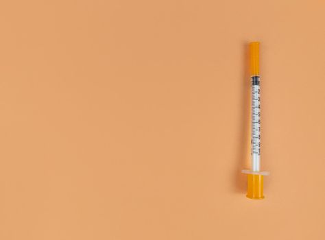 Insulin syringe on an orange background with copy space.