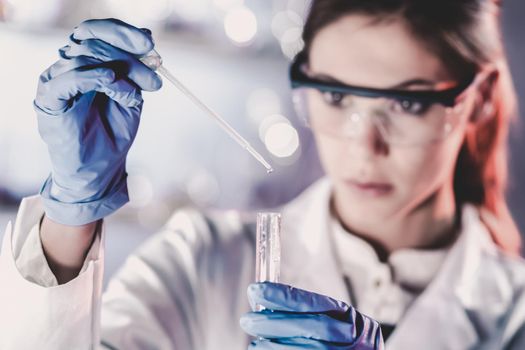 Life scientists researching in laboratory. Focused female life science professional pipetting solution into the glass cuvette. Lens focus on researcher's eyes. Healthcare and biotechnology concept.