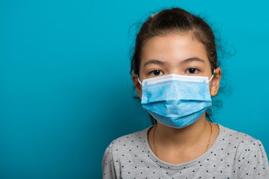 Arabian toddler girl in medical mask on blue background. Close-up.