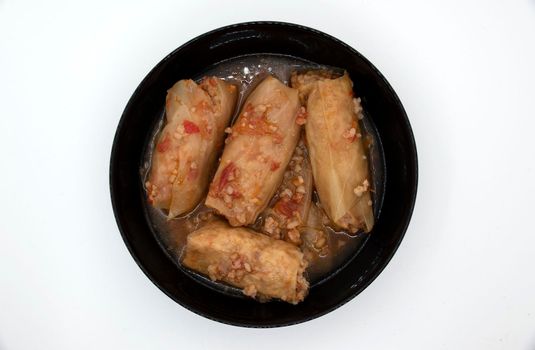 A dish of cabbage rolls in a black plate, which is minced meat with boiled rice, wrapped in cabbage leaves.