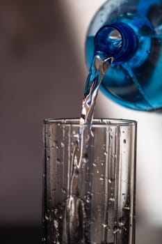 Pouring water from blue plastic bottle into a glass on blurred background. Selective focus, shallow DOF and copy space