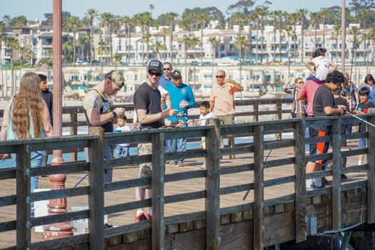 Tourist walking on the Oceanside Pier during blue summer day, Oceanside, northern San Diego County, California. Wooden pier on the western United States coastline. Famous for fisher. March 22nd, 2020