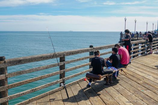 Tourist walking on the Oceanside Pier during blue summer day, Oceanside, northern San Diego County, California. Wooden pier on the western United States coastline. Famous for fisher. March 22nd, 2020