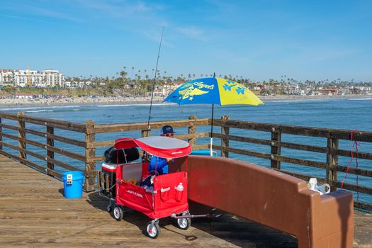 Tourist walking on the Oceanside Pier during blue summer day, Oceanside, northern San Diego County, California. Wooden pier on the western United States coastline. Famous for fisher. March 22nd, 2020