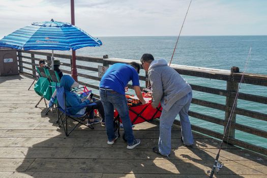 Tourist walking on the Oceanside Pier during blue summer day, Oceanside, northern San Diego County, California. Wooden pier on the western United States coastline. Famous for fisher. March 22nd, 2020