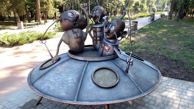 Steel flying saucer with funny aliens in the city park.