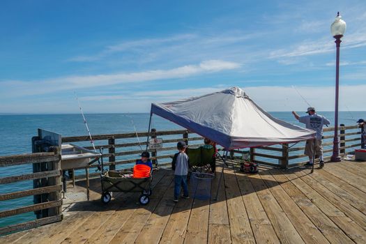 Tourist walking on the Oceanside Pier during blue summer day, Oceanside, northern San Diego County, California. Wooden pier on the western United States coastline. Famous for fisher. March 22nd, 2020